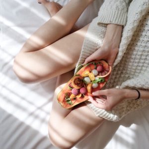 A person holding a papaya fruit on bed for her diet and health.